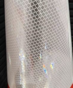 Close-up of a cylindrical object wrapped in a clear film with a white hexagonal grid and iridescent specks on a red background (likely a vinyl sticker or wrap).