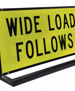 Pillot Vehicle Sign Rig » Highway 1 Bright yellow warning sign reading 'WIDE LOAD FOLLOWS' mounted on a black metal frame and stand.