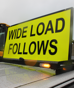 Sign Rig 2 » Highway 1 Bright yellow road sign reading 'WIDE LOAD' on a construction vehicle in a rainy setting with water droplets on the car hood.